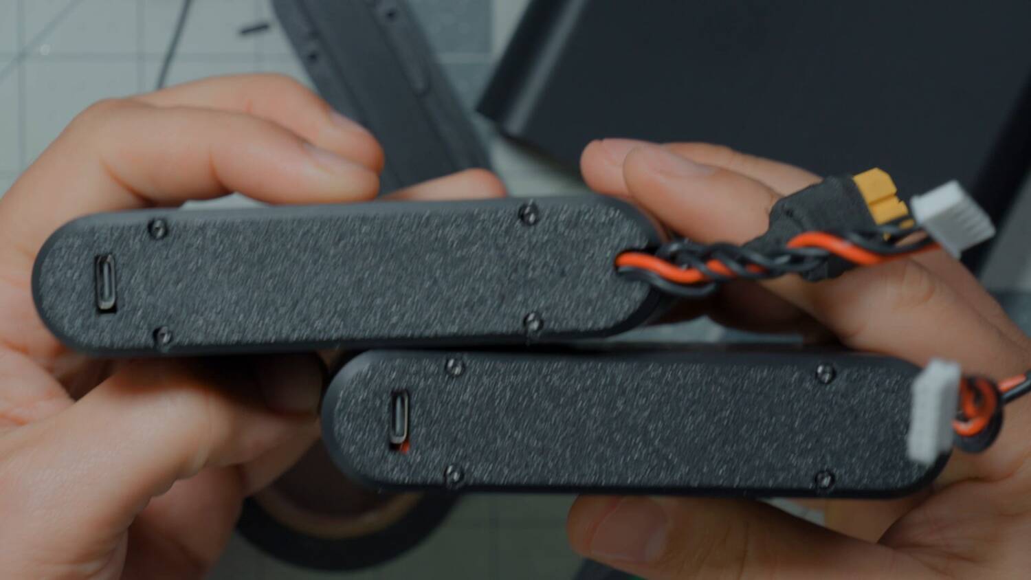Two finished battery packs in black 3D printed cases with USB-C ports and leads