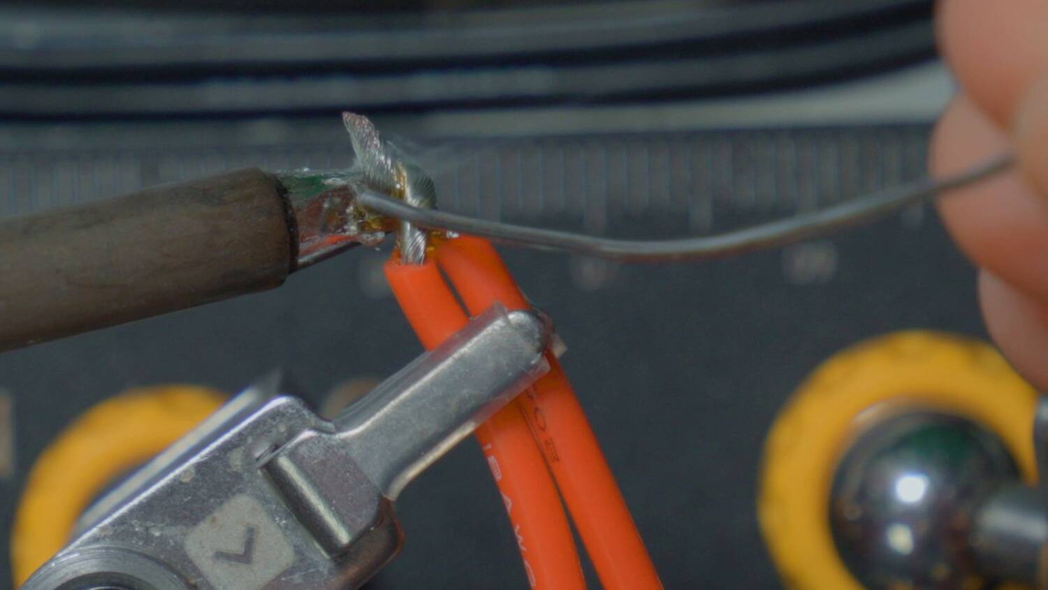 Soldering iron joining the twisted ends of two red 18 gauge wires held in helping hands