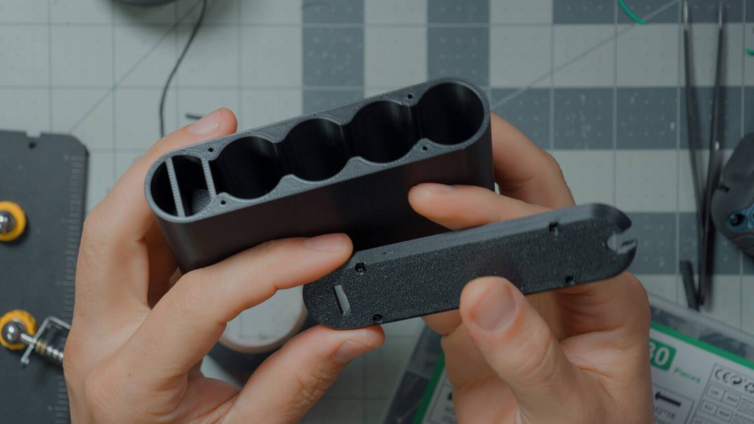Empty black 3D printed battery case with five bays, next to its lid